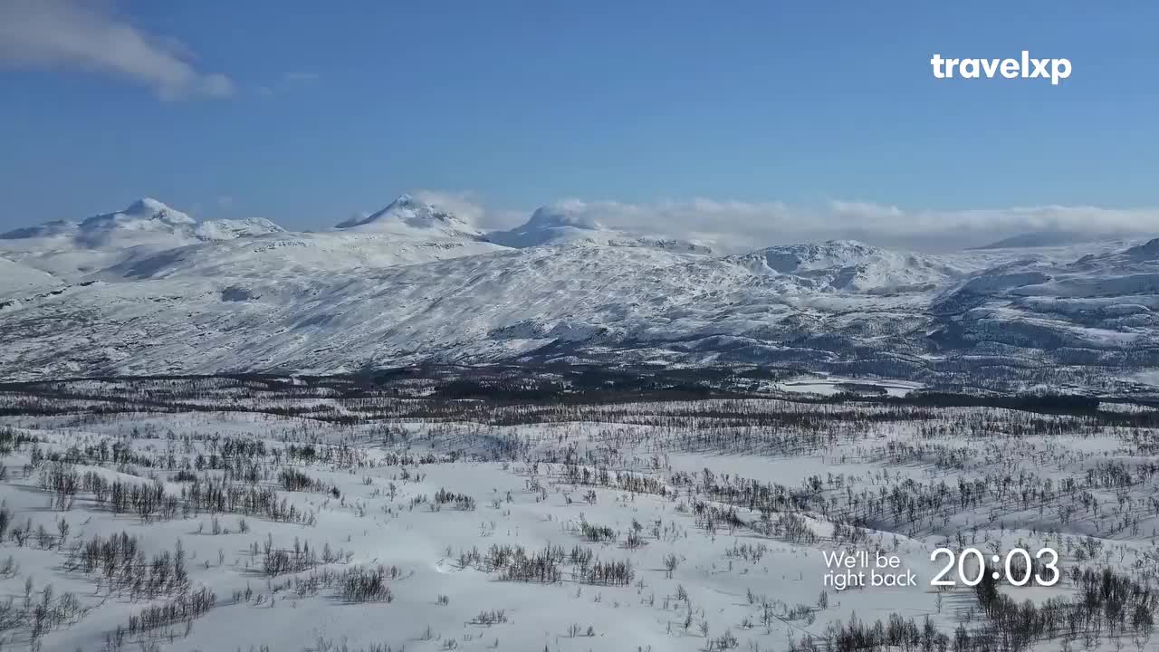 Snow blankets the vast landscape, stretching towards the distant, snow-capped mountains under a bright blue sky. The Travelxp logo and a "We'll be right back" message appear in the lower right corner.
Snow blankets the vast landscape, stretching towards the distant, snow-capped mountains under a bright blue sky. The Travelxp logo and a "We'll be right back" message appear in the lower right corner.