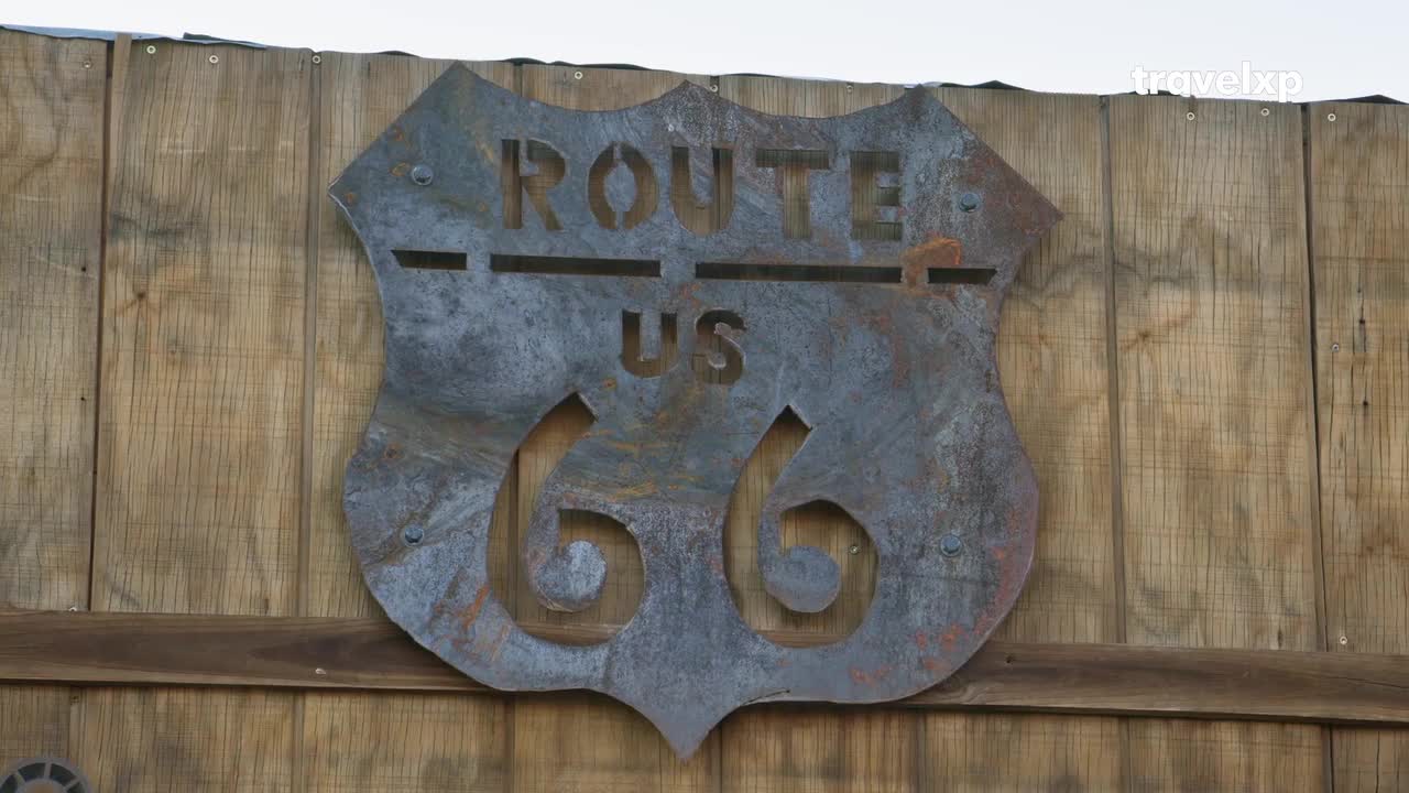 A weathered metal sign for "US Route 66" is bolted to a rustic wooden fence. The sign's cutouts reveal the wood behind it, hinting at a journey through America, much like the travel documentaries on Travelxp. A weathered metal sign for "US Route 66" is bolted to a rustic wooden fence. The sign's cutouts reveal the wood behind it, hinting at a journey through America, much like the travel documentaries on Travelxp.