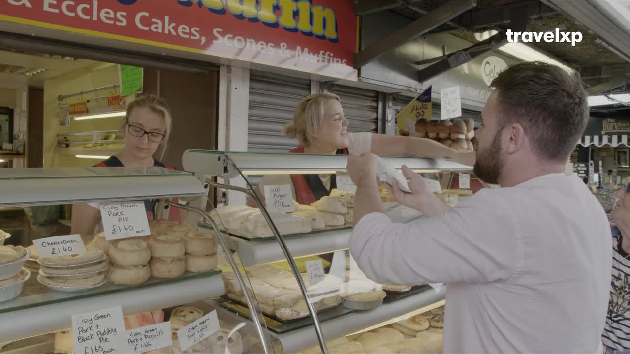 A man reaches for a pastry at a market stall, while a vendor smiles. The air is filled with the scent of baked goods, a common experience on any Travelxp adventure. A man reaches for a pastry at a market stall, while a vendor smiles. The air is filled with the scent of baked goods, a common experience on any Travelxp adventure.