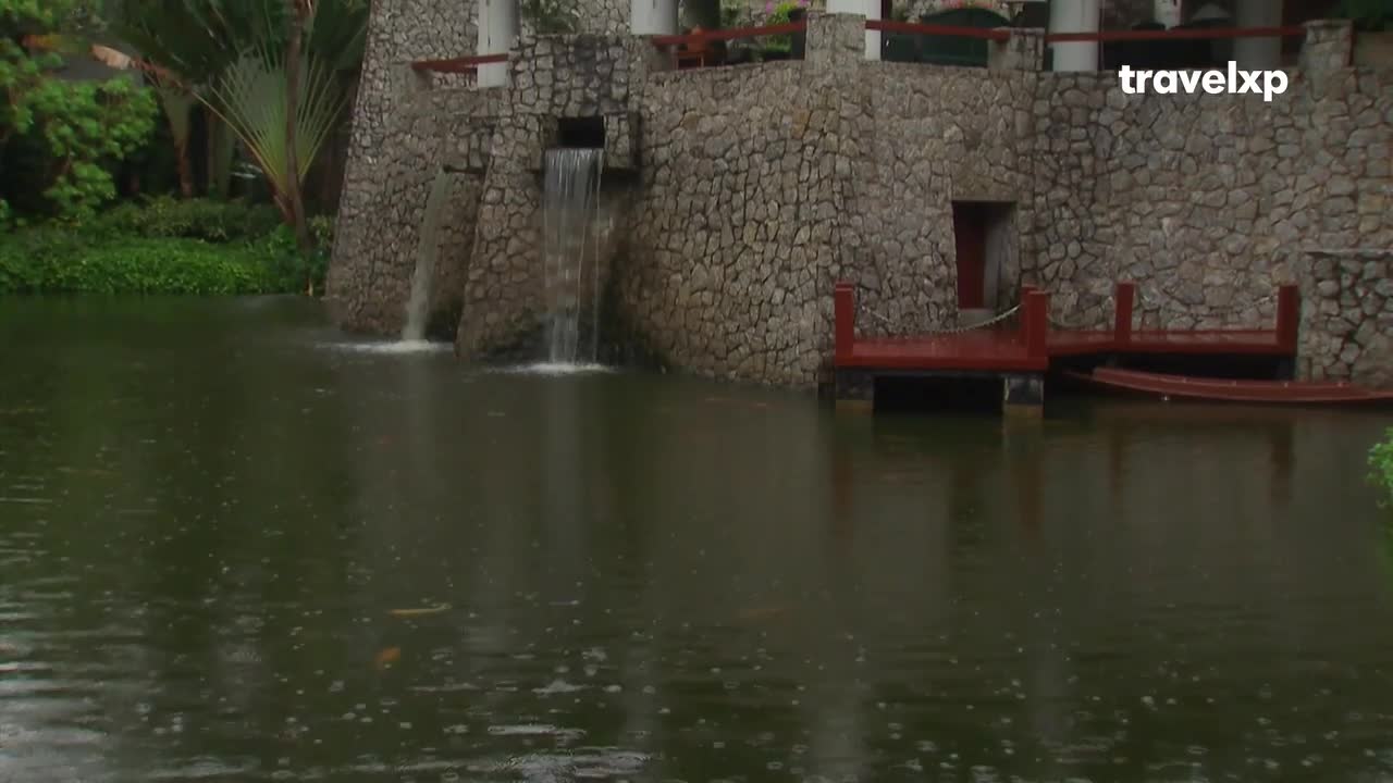 Water tumbles down a stone wall into a dark pond. A narrow, wooden boat rests beside a red dock. Water tumbles down a stone wall into a dark pond. A narrow, wooden boat rests beside a red dock.