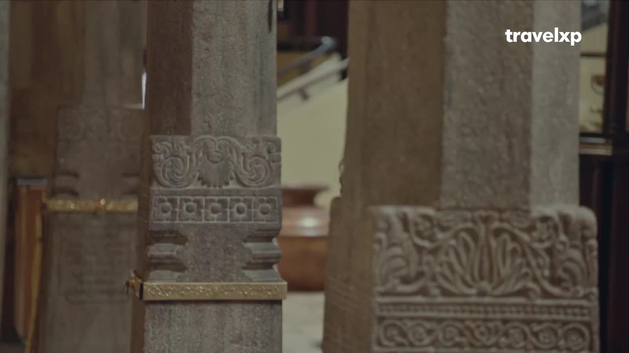 Intricate carvings adorn the stone pillars of this Indian landmark. A glimpse of a large clay pot sits in the background, hinting at the history of this place.