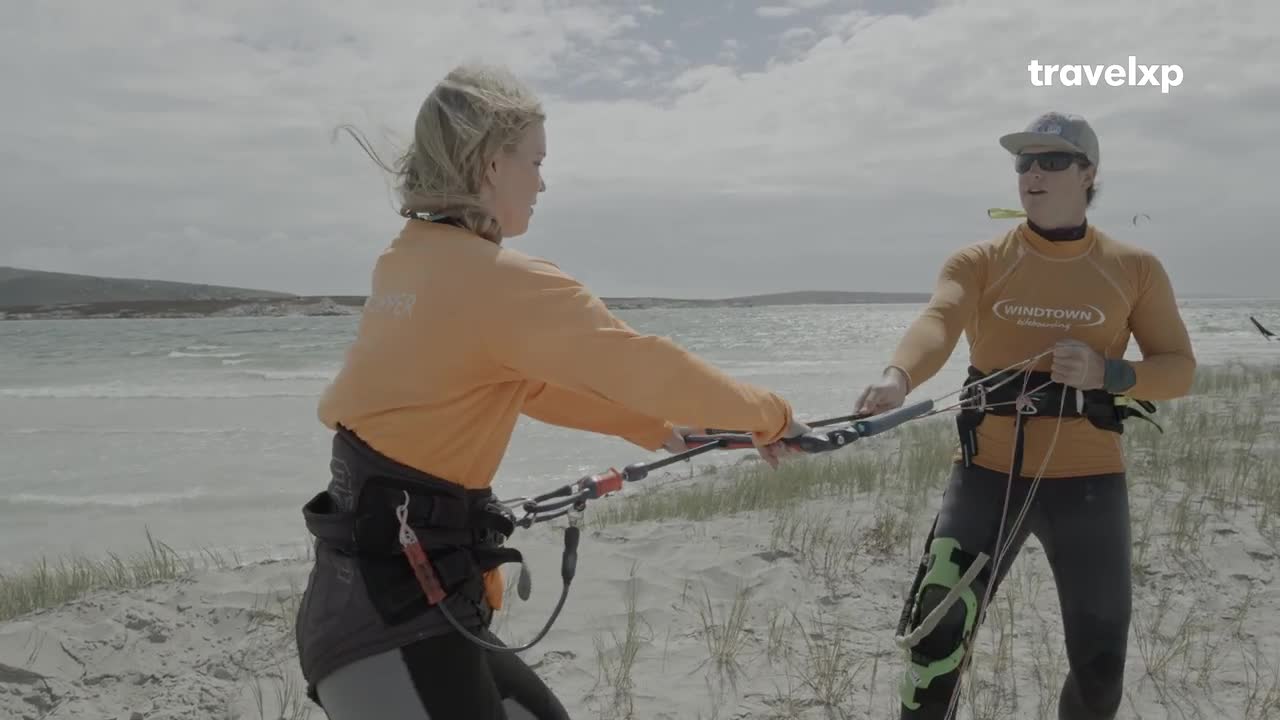 The instructor adjusts the kite bar, guiding the student through the setup on this breezy Indian beach. The water behind them is choppy, hinting at the conditions for their upcoming kitesurfing adventure.