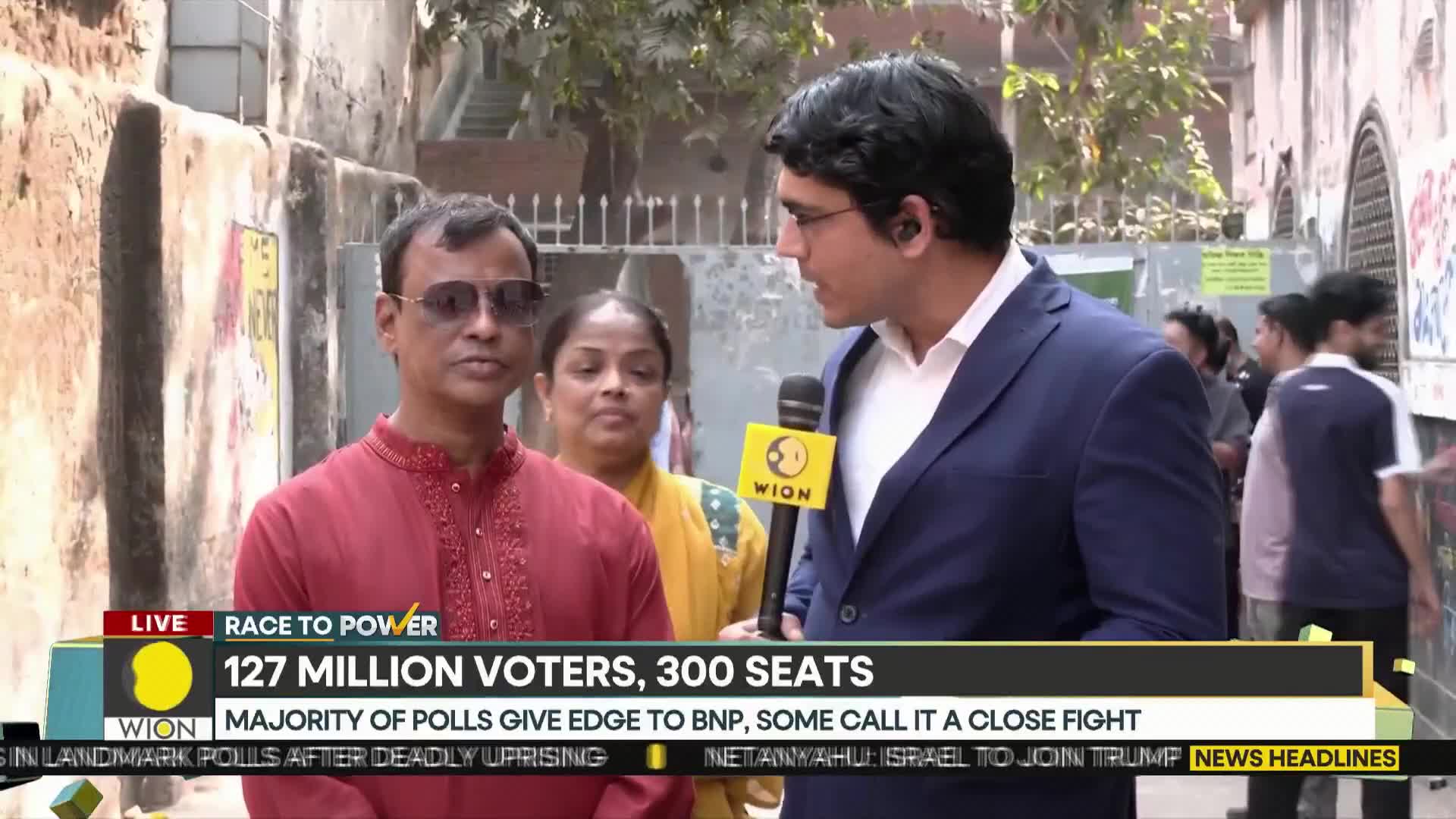 A WION reporter holds a microphone towards a man in a red kurta, who stands with a woman in a yellow sari. The news ticker below them reports on India's election, with 127 million voters and 300 seats at stake.