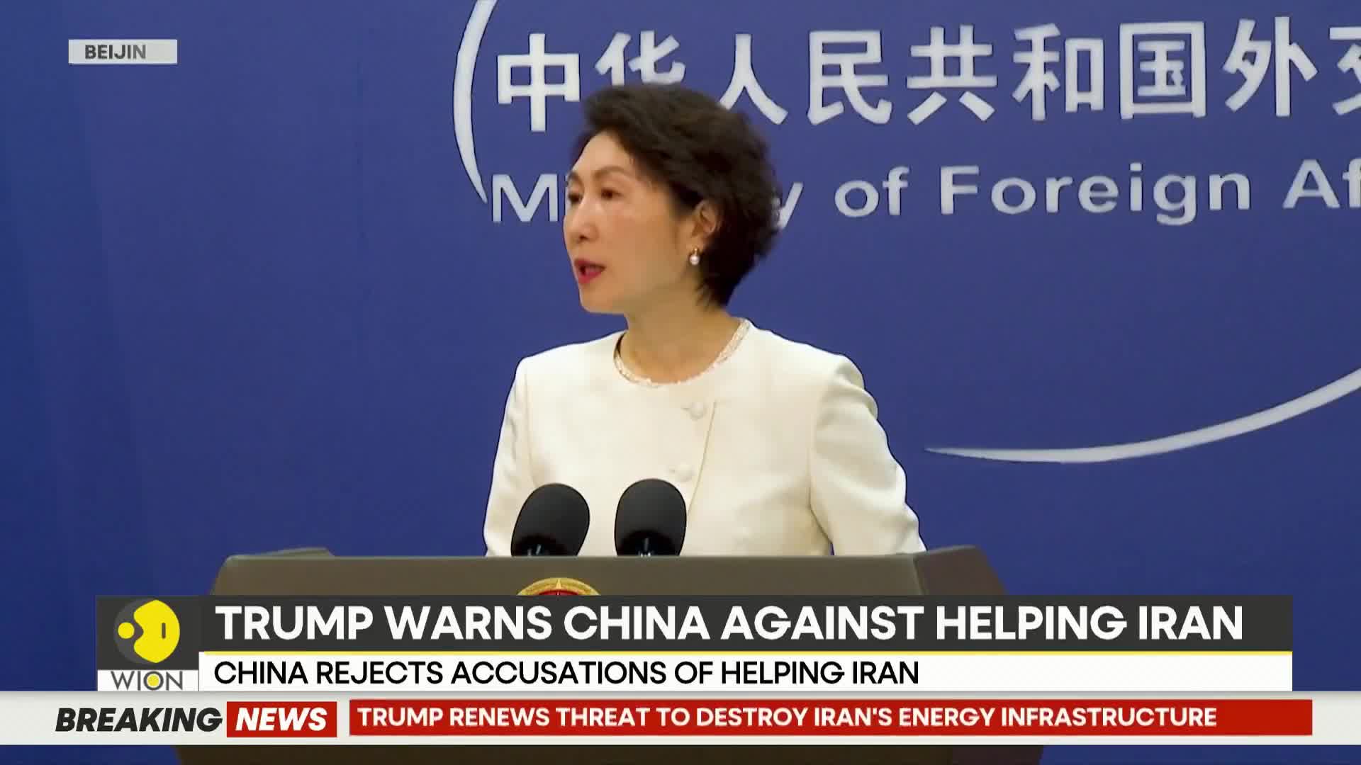 A woman in a white suit stands at a podium, speaking into two microphones. A blue banner behind her displays Chinese characters and "Ministry of Foreign Affairs." Below, a WION news ticker scrolls with headlines about Trump, China, and Iran.