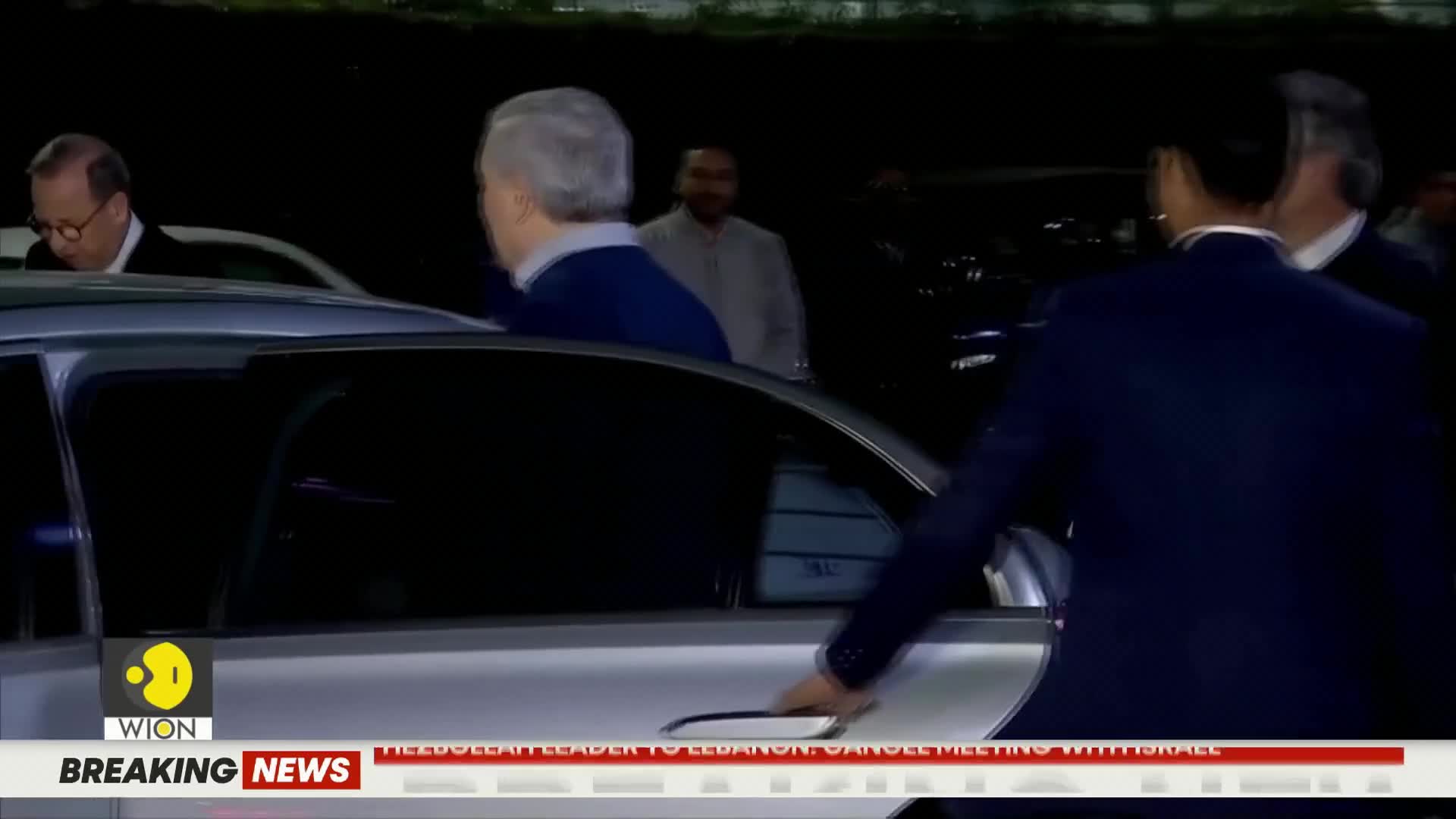 A man in a dark suit opens the car door for a distinguished gentleman in a blue sweater. The WION breaking news chyron scrolls across the bottom of the screen.