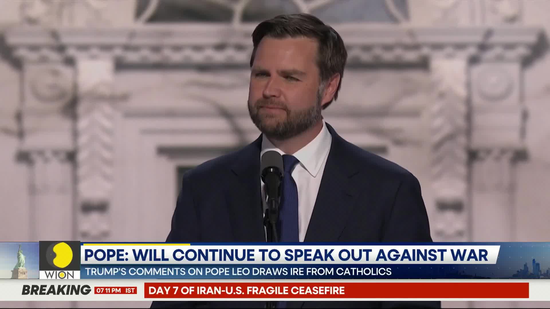 A man in a dark suit stands at a podium, speaking into a microphone. A news ticker at the bottom of the screen displays "WION" and headlines about the Pope and an Iran-U.S. ceasefire.