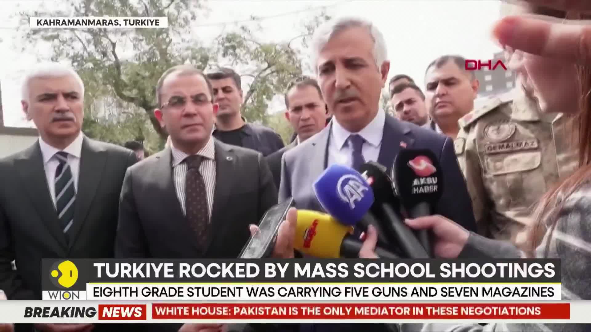 A man in a suit speaks into a cluster of microphones, his expression serious. Behind him, other men in suits and military uniforms stand, some looking towards the camera. A news ticker at the bottom displays "TURKIYE ROCKED BY MASS SCHOOL SHOOTINGS."