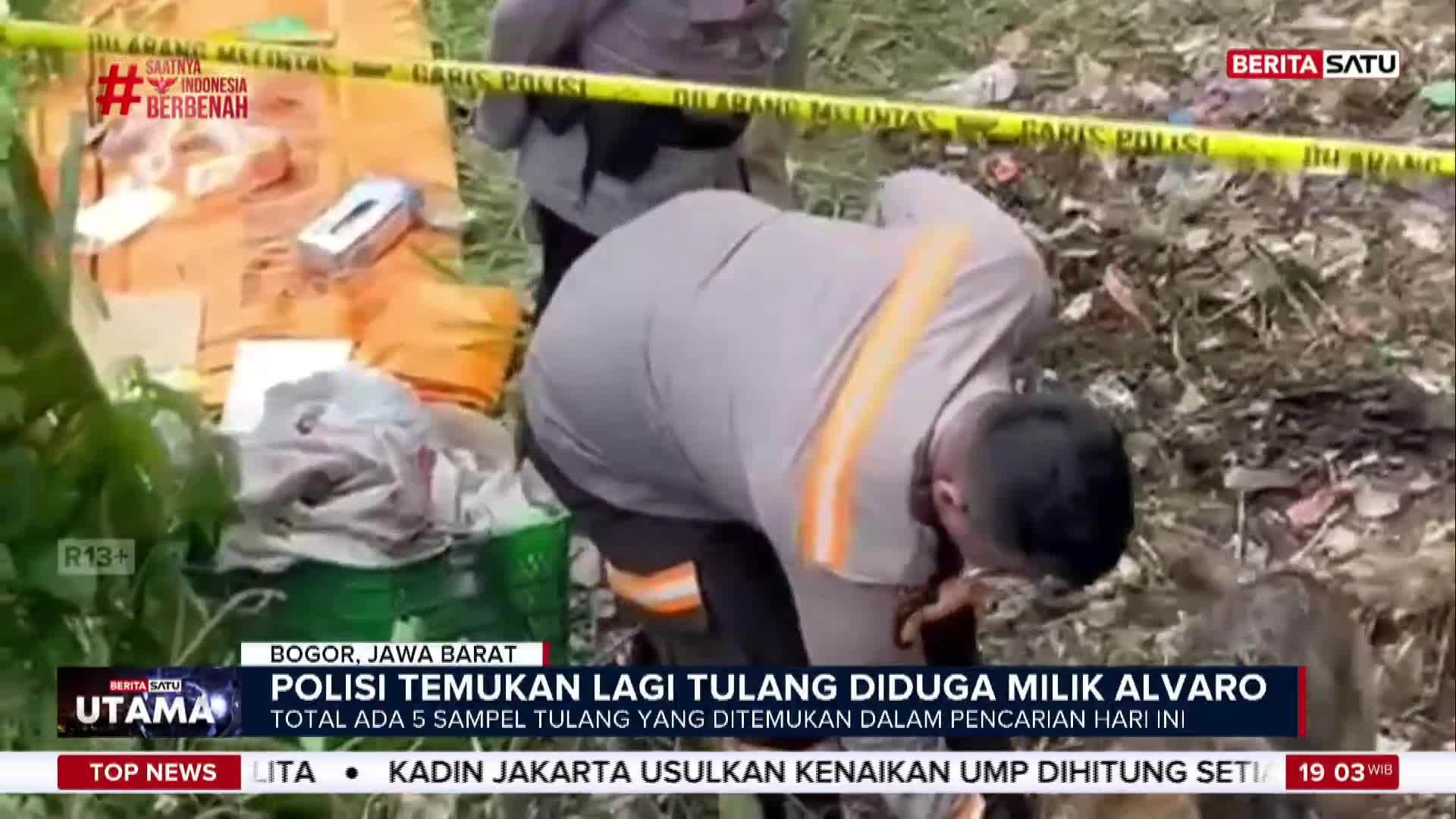 A police officer, in a gray uniform with orange accents, bends over, examining something on the ground. Yellow police tape marks off the scene, as reported by BeritaSatu English in Indonesia.
