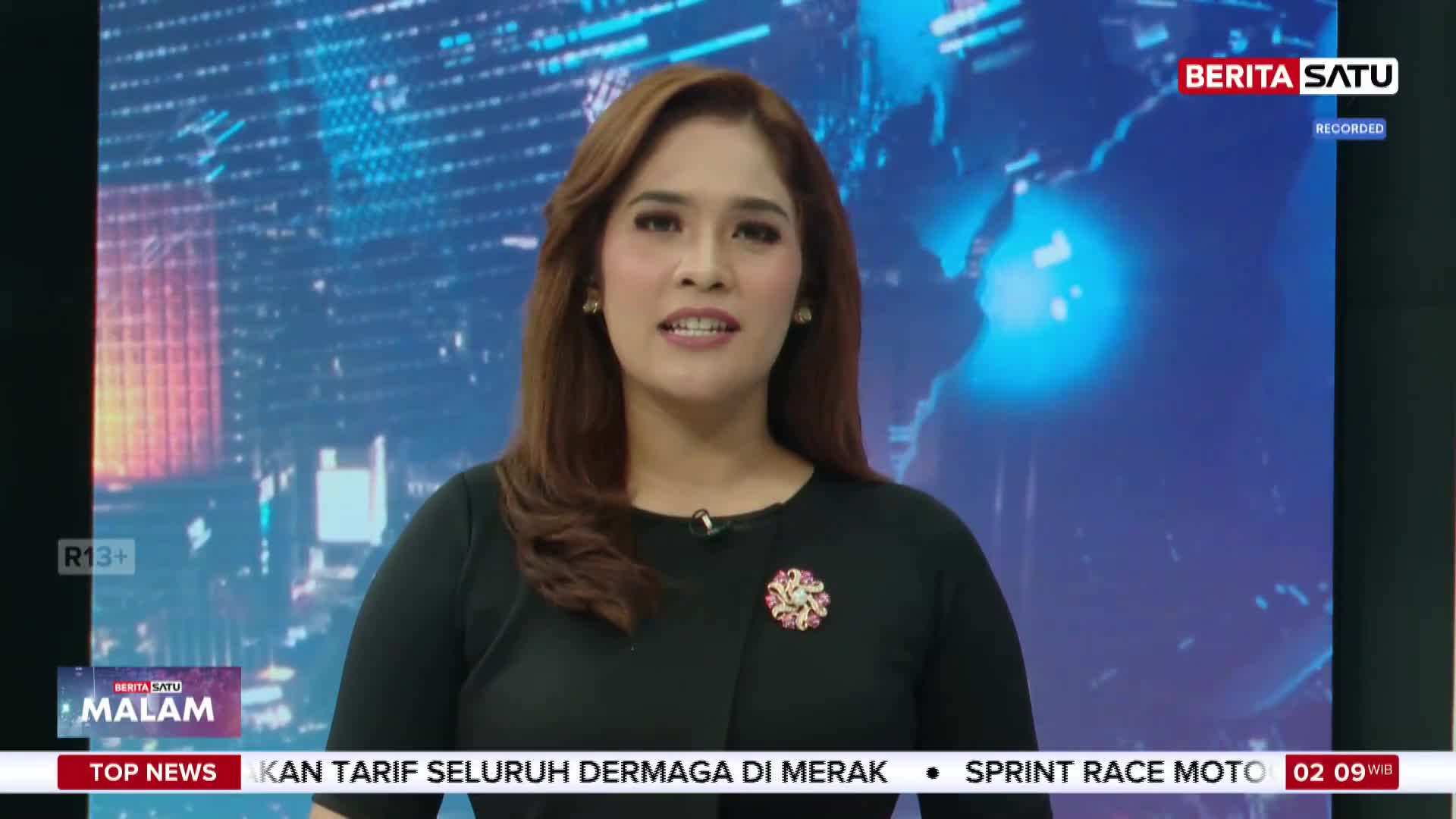 A woman in a black dress stands before a blue, digital map of the world, speaking into a microphone. The Berita Satu logo is visible in the upper right corner, and a ticker tape scrolls across the bottom of the screen. A woman in a black dress stands before a blue, digital map of the world, speaking into a microphone. The Berita Satu logo is visible in the upper right corner, and a ticker tape scrolls across the bottom of the screen.