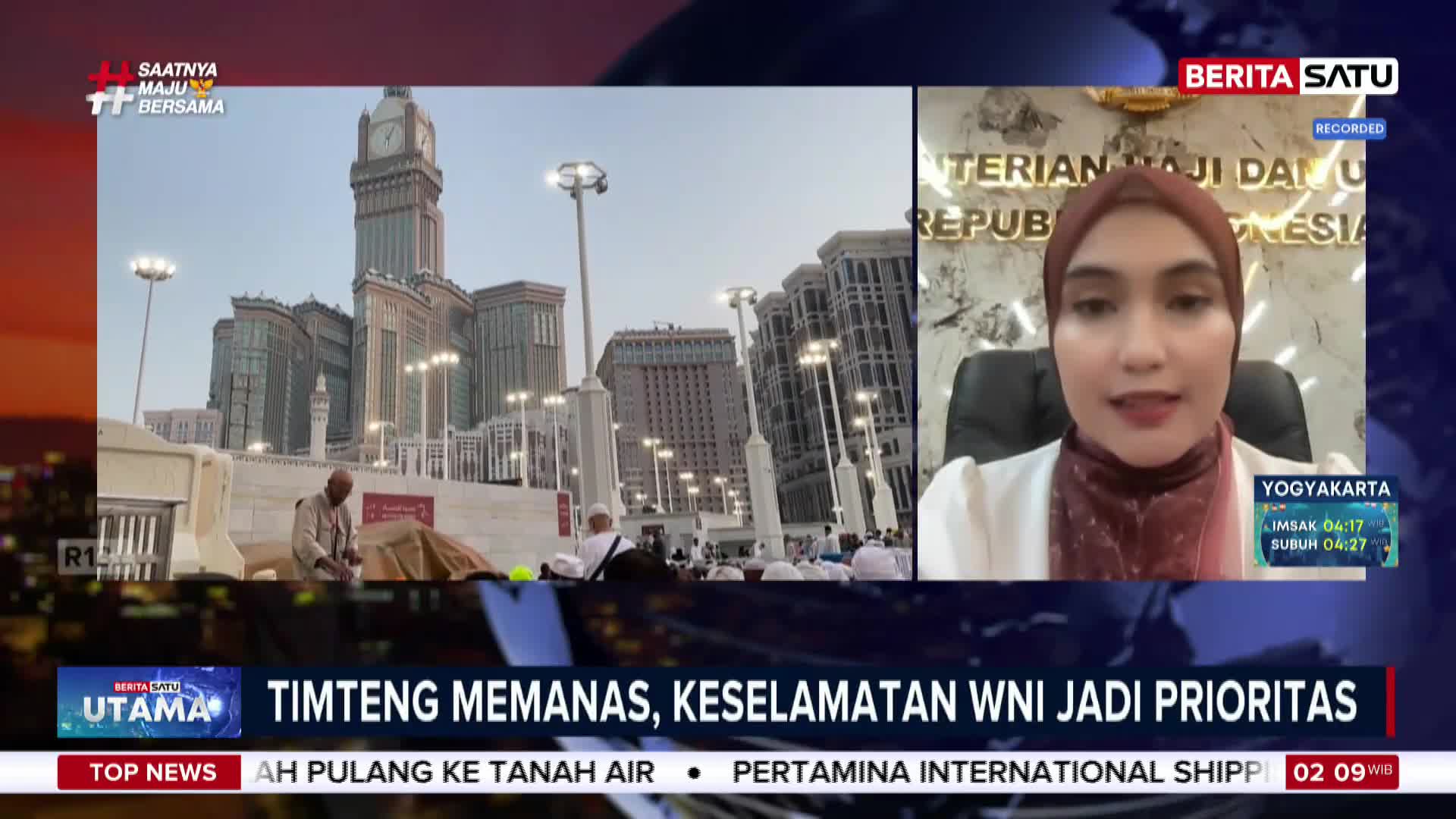Pilgrims in white robes gather near tall buildings in Mecca, with a man in the foreground tending to something on the ground. A woman in a hijab speaks from a screen, her words about the safety of Indonesian citizens likely being broadcast by BeritaSatu. Pilgrims in white robes gather near tall buildings in Mecca, with a man in the foreground tending to something on the ground. A woman in a hijab speaks from a screen, her words about the safety of Indonesian citizens likely being broadcast by BeritaSatu.