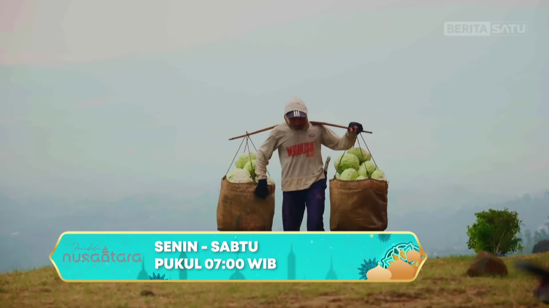 A farmer walks across a misty hillside, balancing two large sacks of cabbage on a shoulder pole. The BeritaSatu logo appears in the upper right corner.
