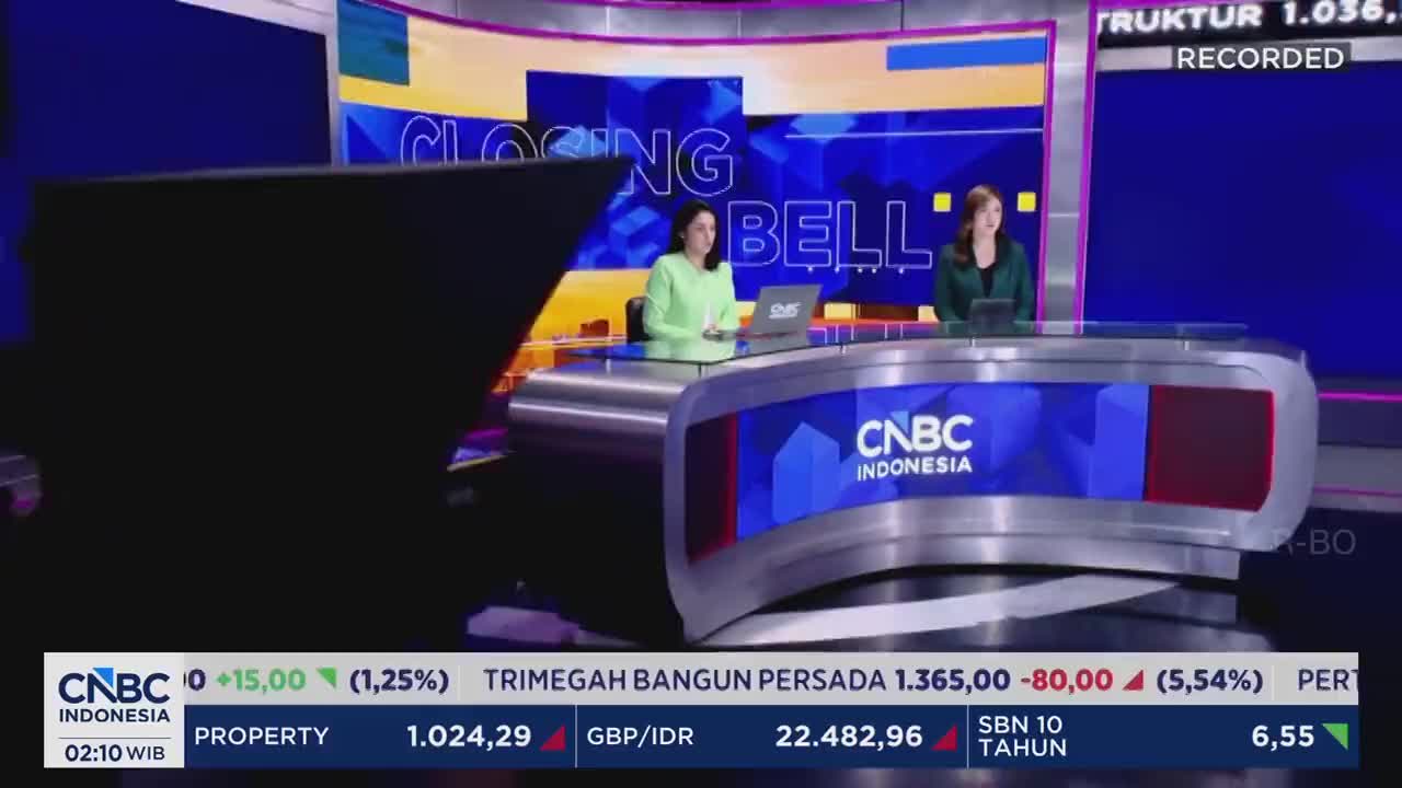 Two women sit at a curved desk in front of a large screen displaying "CLOSING BELL." A ticker runs along the bottom of the screen, showing financial data from CNBC Indonesia.