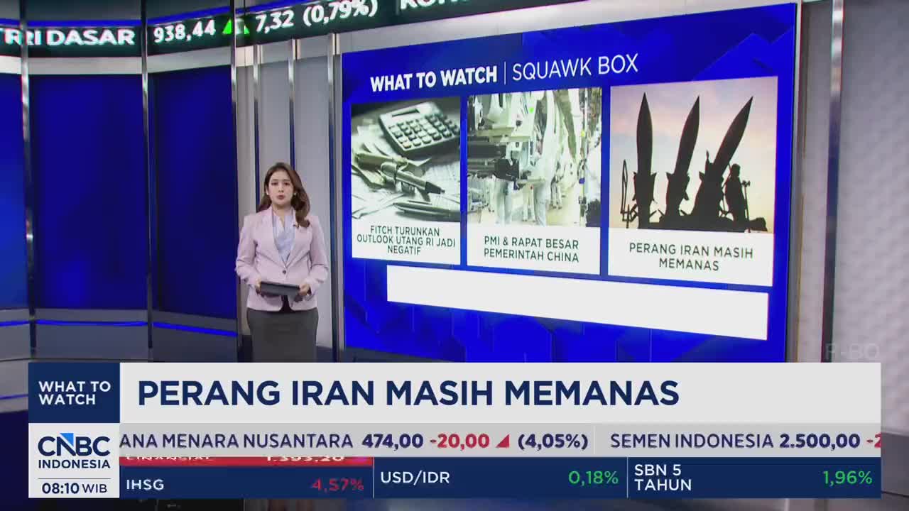 A woman in a light pink blazer stands before a large screen displaying financial news from CNBC Indonesia. Silhouetted missiles dominate the right side of the screen, illustrating the ongoing tensions in Iran.