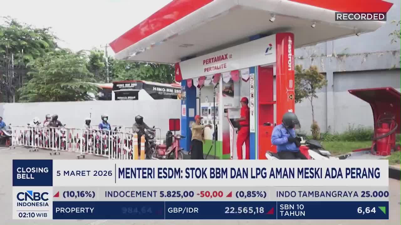 Motorcyclists wait in line at a Pertamina gas station in Indonesia. A worker in red fills a customer's tank while another stands by a payment terminal.