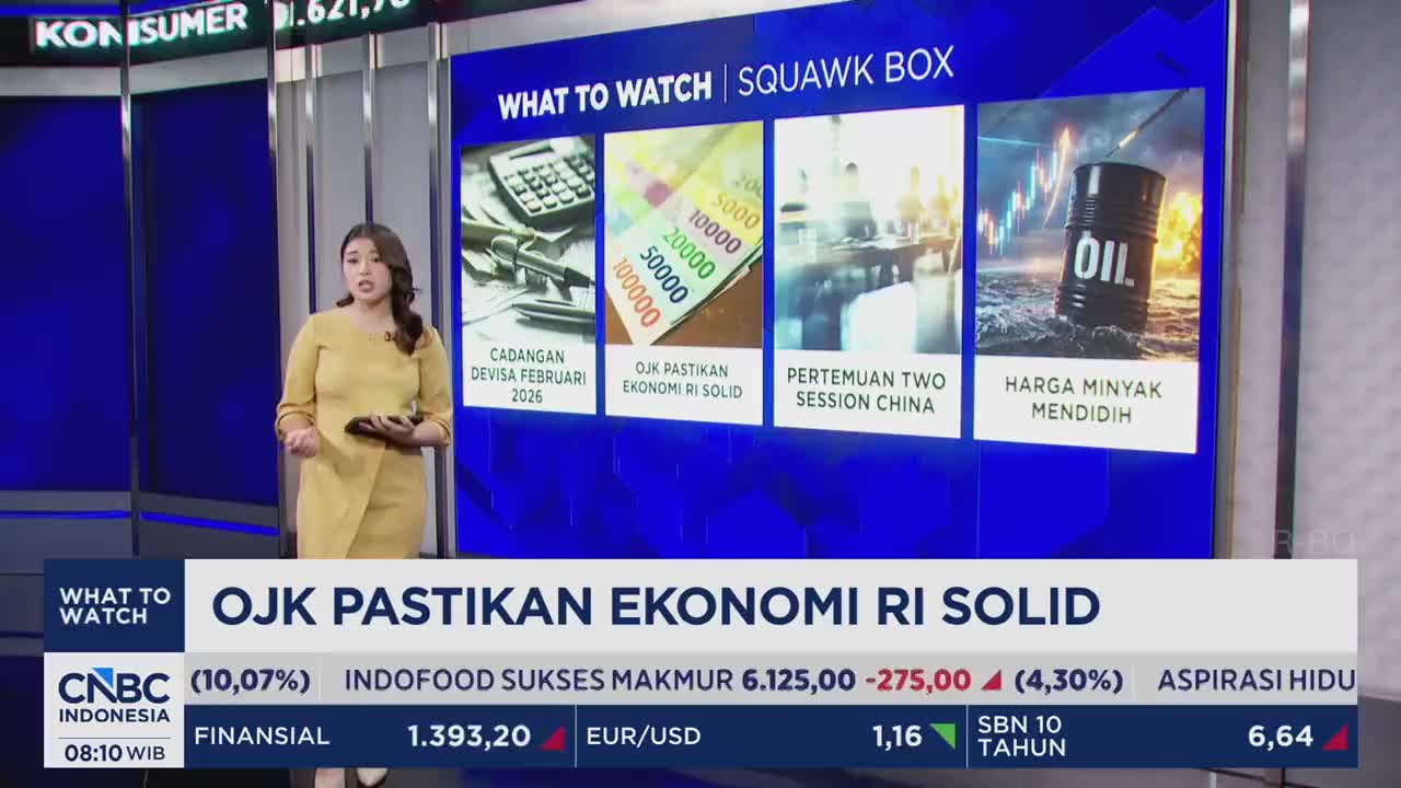 A woman in a yellow dress stands beside a screen displaying financial news from CNBC Indonesia. The screen highlights "OJK Pastikan Ekonomi RI Solid," indicating confidence in Indonesia's economy.