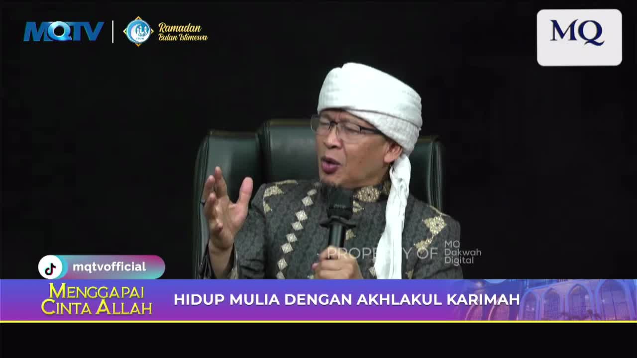 A man in a white turban and patterned robe speaks into a microphone, gesturing with his hands. The MQTV logo appears in the upper corner, and text on the screen reads "HIDUP MULIA DENGAN AKHLAKUL KARIMAH."