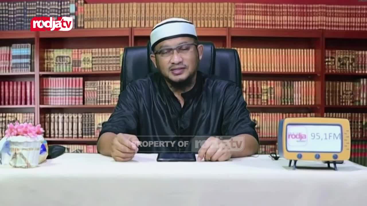 A man in a peci hat and black shirt speaks from behind a desk, his hands resting on the surface. Behind him, shelves packed with books line the walls, and a small, retro-style radio displays "rodja 95.1 FM."