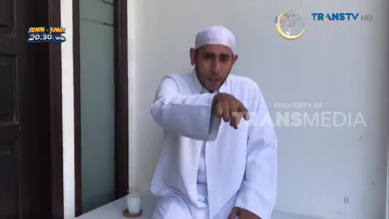 A man in a white peci and robe gestures emphatically towards the camera. The Trans TV logo is visible in the background, indicating this is a broadcast from Indonesia. A man in a white peci and robe gestures emphatically towards the camera. The Trans TV logo is visible in the background, indicating this is a broadcast from Indonesia.