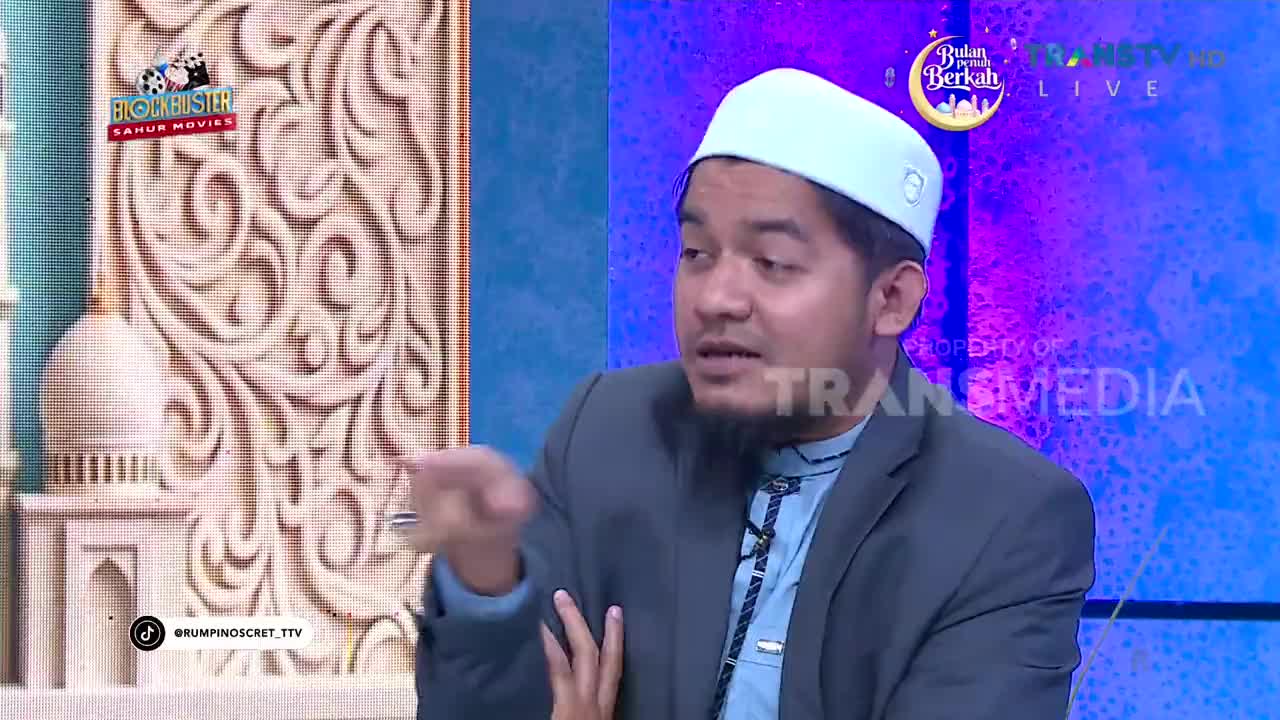 A man in a white peci and gray suit gestures with his left hand, speaking animatedly. The Trans TV logo appears on the screen behind him.