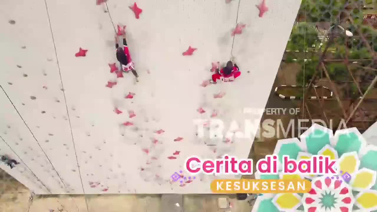 Two climbers ascend a sheer wall dotted with red star-shaped holds. Below them, a banner for Trans7's "Cerita di Balik Kesuksesan" unfurls.