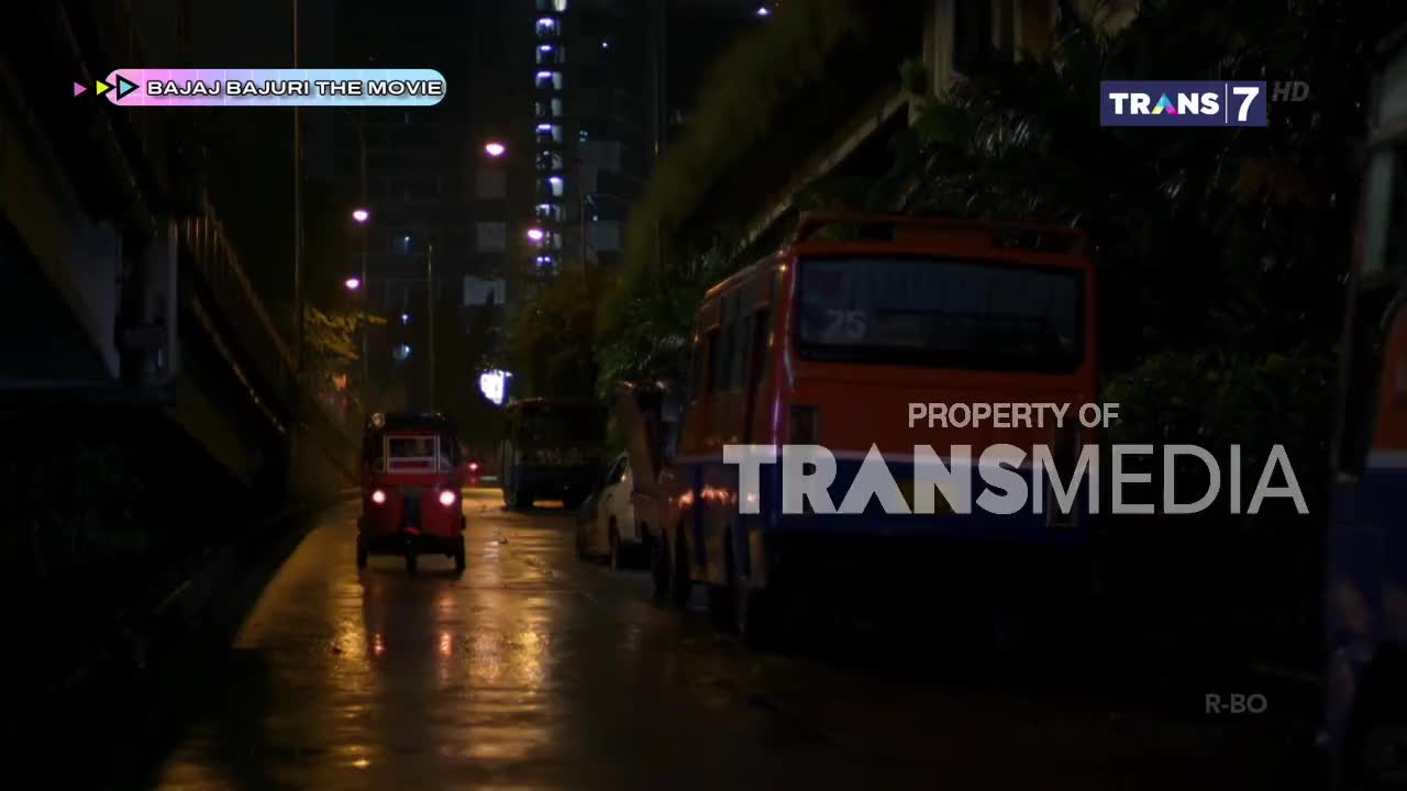 A bright red bajaj is moving down a wet street at night, reflecting the streetlights. Behind it, a large orange bus, likely part of the Trans7 broadcast, is parked. A bright red bajaj is moving down a wet street at night, reflecting the streetlights. Behind it, a large orange bus, likely part of the Trans7 broadcast, is parked.