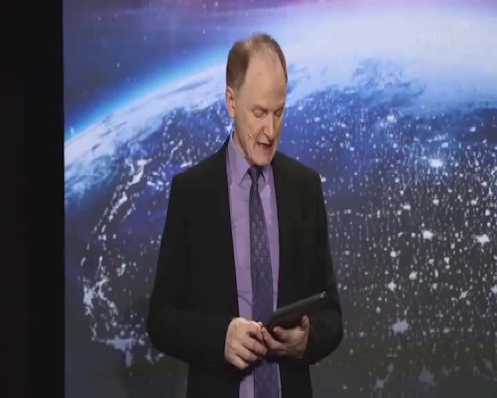The man in the suit is looking down, holding a tablet. Behind him, a backdrop of a nighttime Earth scene glows.

