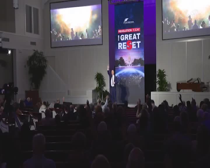 A man in a suit stands on a stage, waving to a congregation with their hands raised. A large screen behind him displays images of a globe and text that reads "REVELATION TODAY THE GREAT RESET." A man in a suit stands on a stage, waving to a congregation with their hands raised. A large screen behind him displays images of a globe and text that reads "REVELATION TODAY THE GREAT RESET."