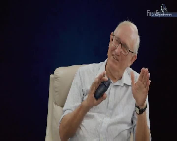 A man in a light blue striped shirt gestures with both hands, holding a dark object in his left. He's leaning forward, his mouth open as if speaking. A man in a light blue striped shirt gestures with both hands, holding a dark object in his left. He's leaning forward, his mouth open as if speaking.