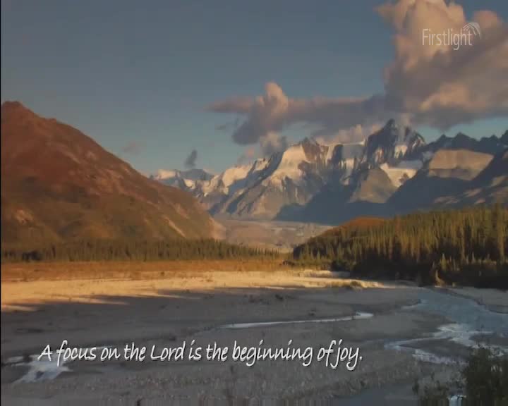 The sun's first light catches the snow-capped peaks of the Southern Alps. A braided river winds through a valley carpeted in tussock and beech forest.