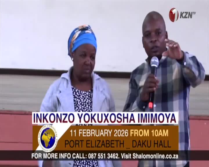 A man speaks into a microphone, gesturing with his free hand. Beside him, a woman stands with a serious expression. A banner below them announces an event in Port Elizabeth.