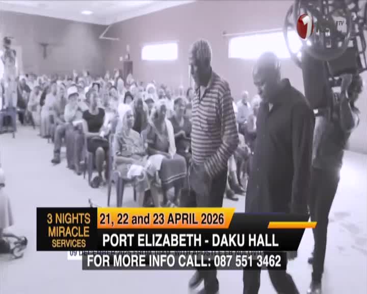 Two men walk past a seated congregation in Port Elizabeth. A camera crew from 1KZN TV is filming the event.