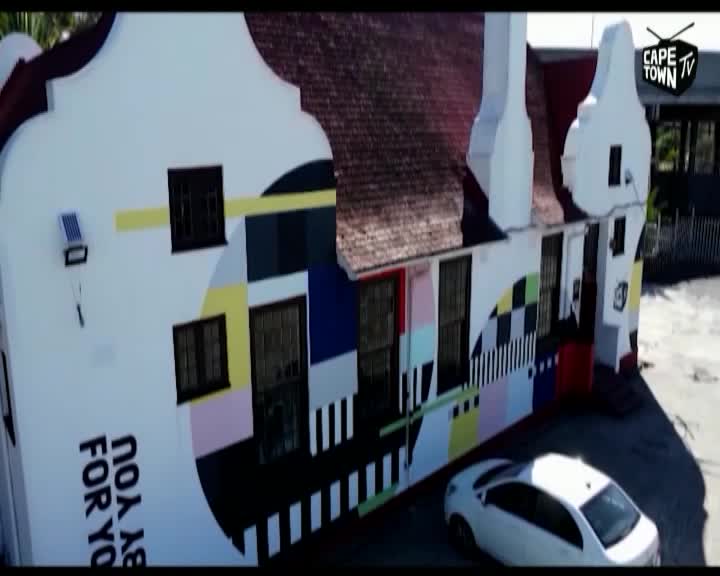 A white sedan is parked in front of a building covered in a vibrant, geometric mural. The Cape Town TV logo is visible in the upper right corner.