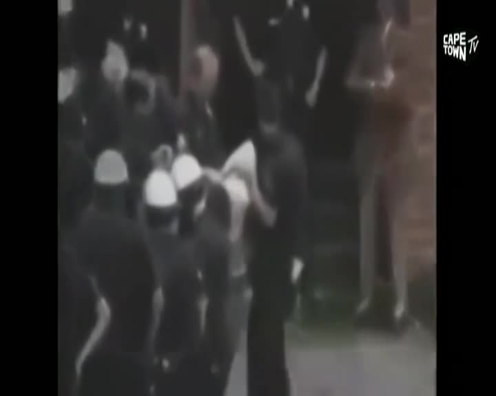 A group of men in dark uniforms, some wearing white helmets, are surrounding another man. One of the uniformed men is holding the other man's arm. The Cape Town TV logo is visible in the corner.