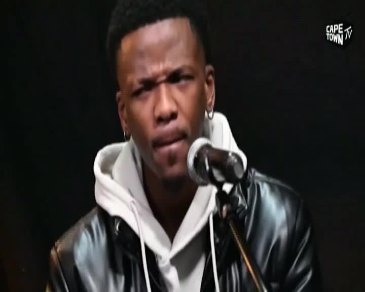 A young man in a black leather jacket and white hoodie leans into a microphone. The Cape Town TV logo appears in the upper right corner.