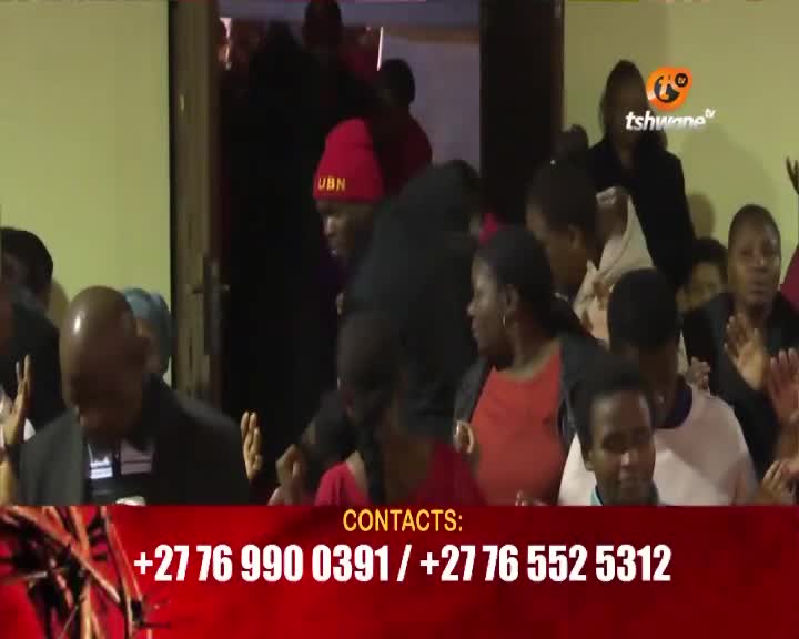 A man in a red beanie with "UBN" on it moves through a doorway. People in the foreground have their hands raised. A man in a red beanie with "UBN" on it moves through a doorway. People in the foreground have their hands raised.