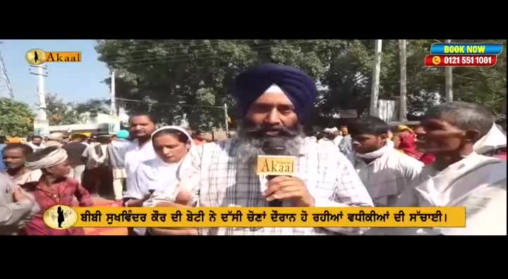 A man in a turban, holding an Akaal microphone, speaks to the camera, surrounded by a crowd of people. Behind him, a banner with text in Punjabi scrolls along the bottom of the screen.
