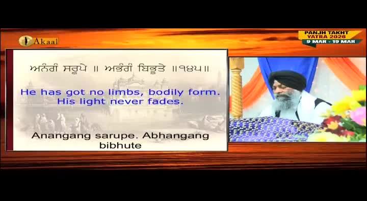 A man with a white beard and a black turban sits at a table, likely speaking on the Akaal Channel. A screen displays text in both Punjabi and English, with a backdrop of a golden hue.
