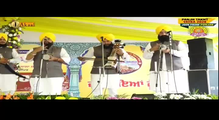 Four men in turbans and traditional dress stand on a stage, playing instruments and singing. The Akaal Channel logo is visible, and the banner indicates a religious event.
