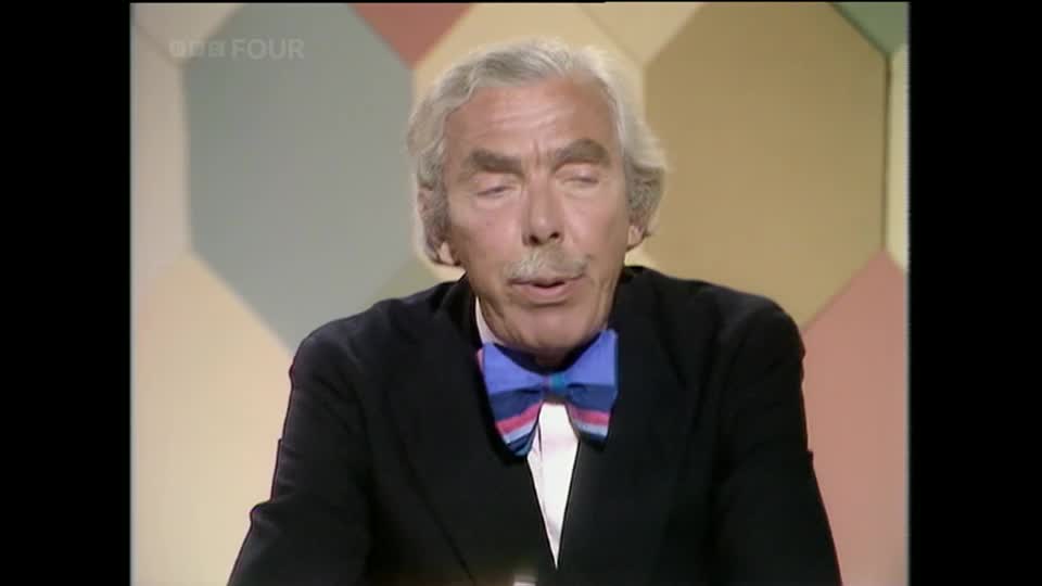 A man with grey hair and a moustache, wearing a dark suit and a striking blue bow tie, speaks directly to the camera. The BBC Four logo appears in the top left corner of the screen.