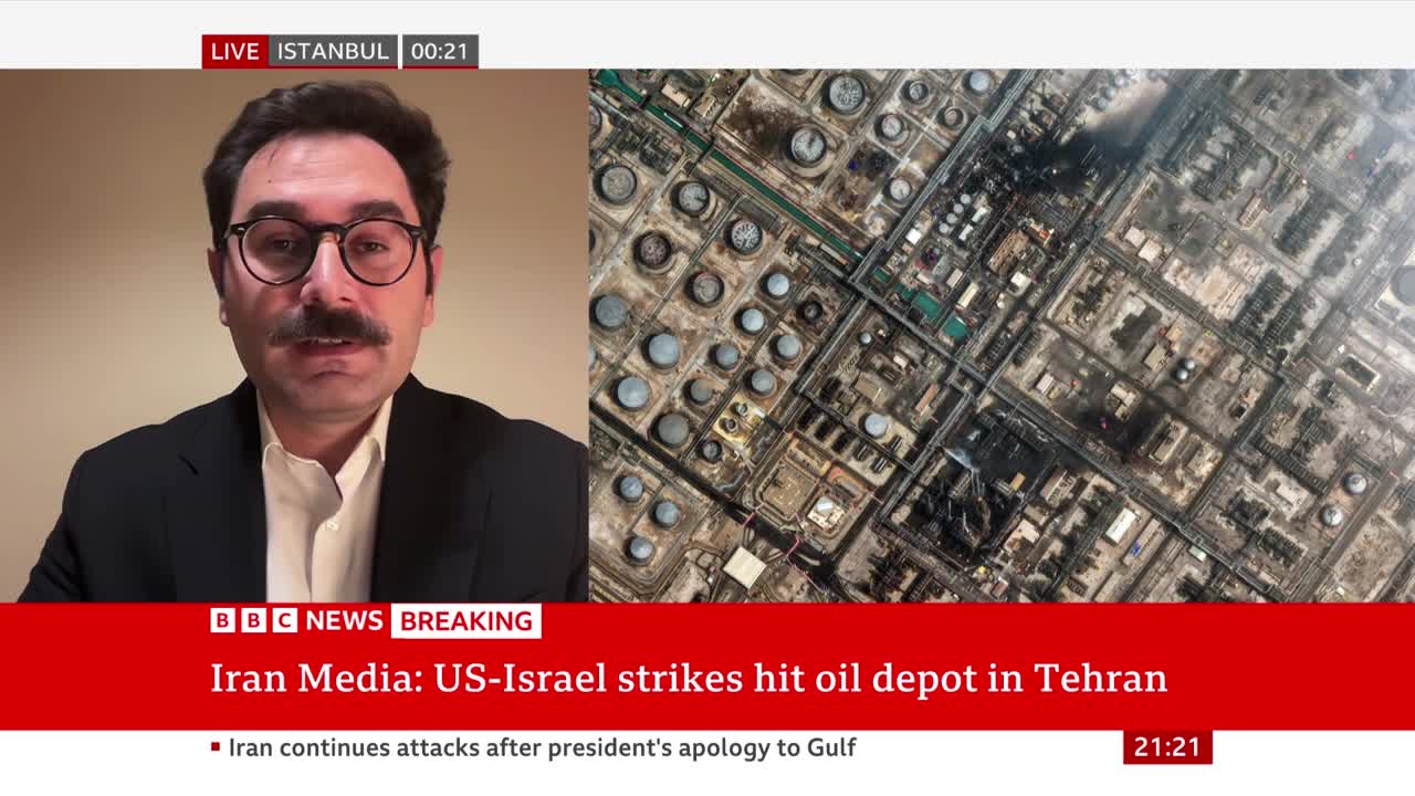 A man with a mustache and glasses is speaking on a BBC News broadcast. An aerial view of an oil depot shows many large, circular storage tanks and industrial buildings. A man with a mustache and glasses is speaking on a BBC News broadcast. An aerial view of an oil depot shows many large, circular storage tanks and industrial buildings.
