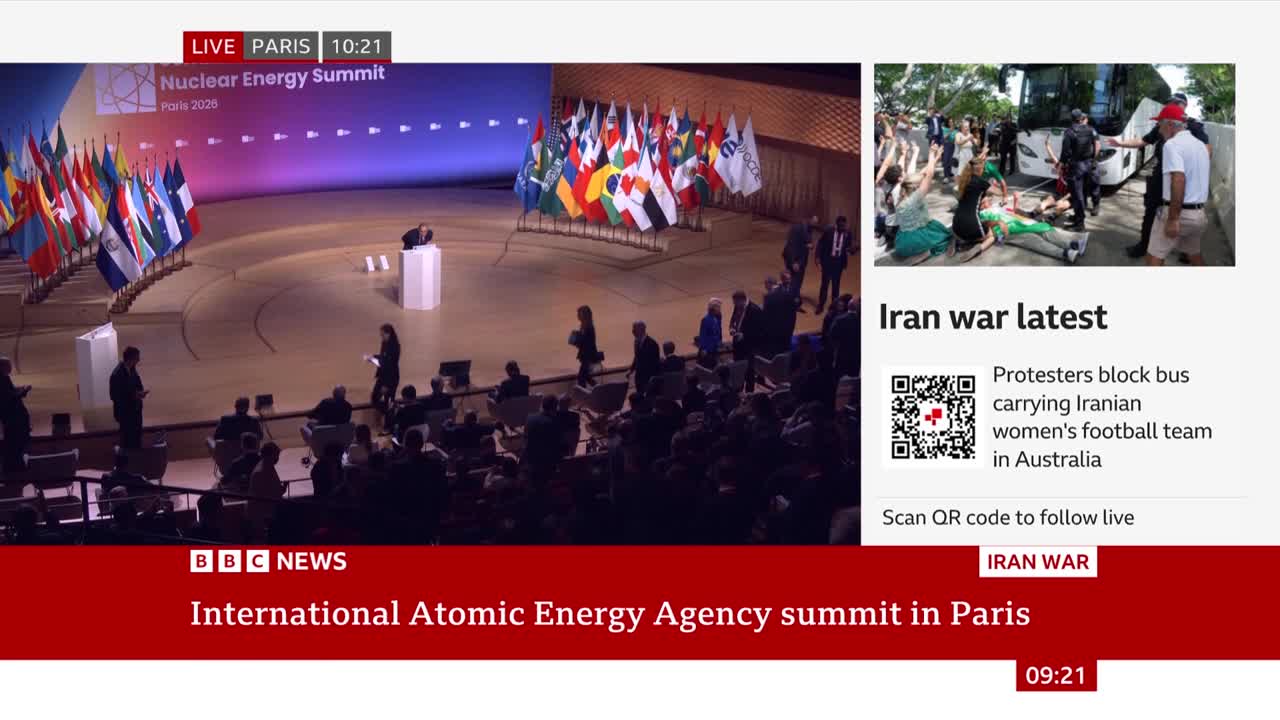 A speaker stands at a podium before a line of national flags at the Nuclear Energy Summit in Paris. On the right, protesters are blocking a bus carrying the Iranian women's football team. A speaker stands at a podium before a line of national flags at the Nuclear Energy Summit in Paris. On the right, protesters are blocking a bus carrying the Iranian women's football team.