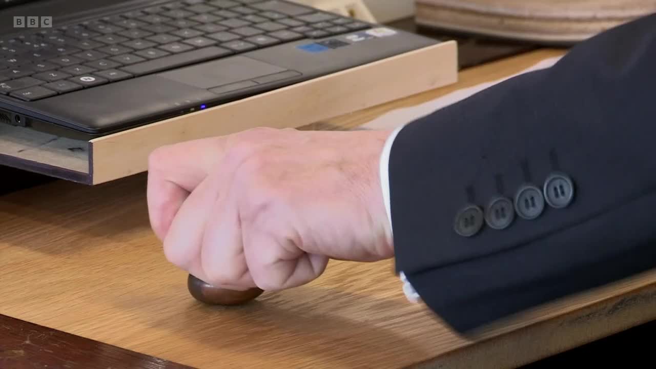 A hand grips a wooden knob, poised above a desk. The BBC Two logo is visible in the corner of the screen.