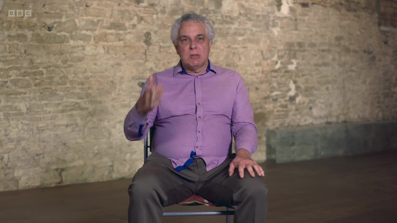 A man in a lavender shirt gestures with his right hand as he speaks. The BBC Two logo is visible in the corner, suggesting this is from a UK broadcast.