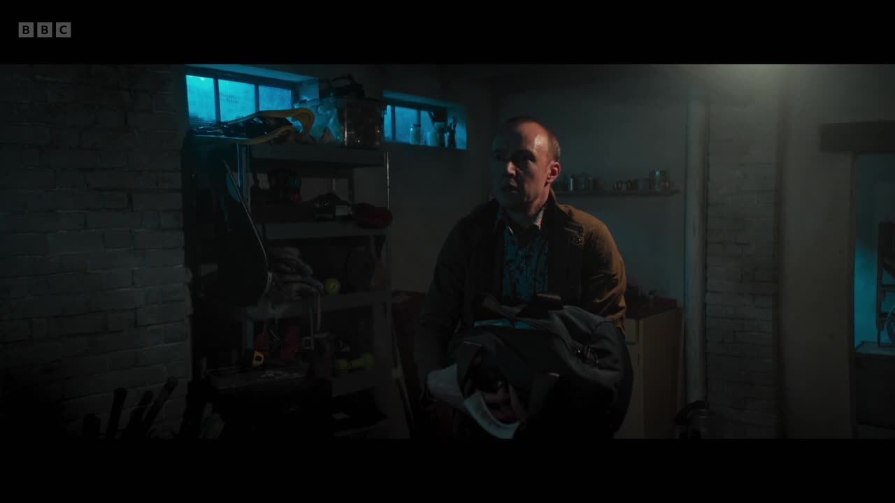A man stands in a dimly lit room, holding a dark jacket. The BBC Two logo is visible in the top left corner.