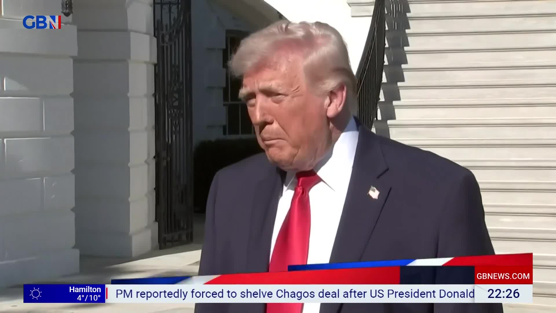 Donald Trump stands outside, his suit jacket slightly open. A news ticker from GB News scrolls across the bottom of the screen.