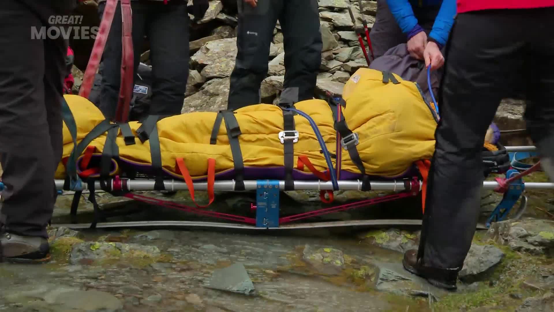 A team carefully carries a person on a stretcher over rocky terrain. Their bright yellow sleeping bag stands out against the rugged landscape.