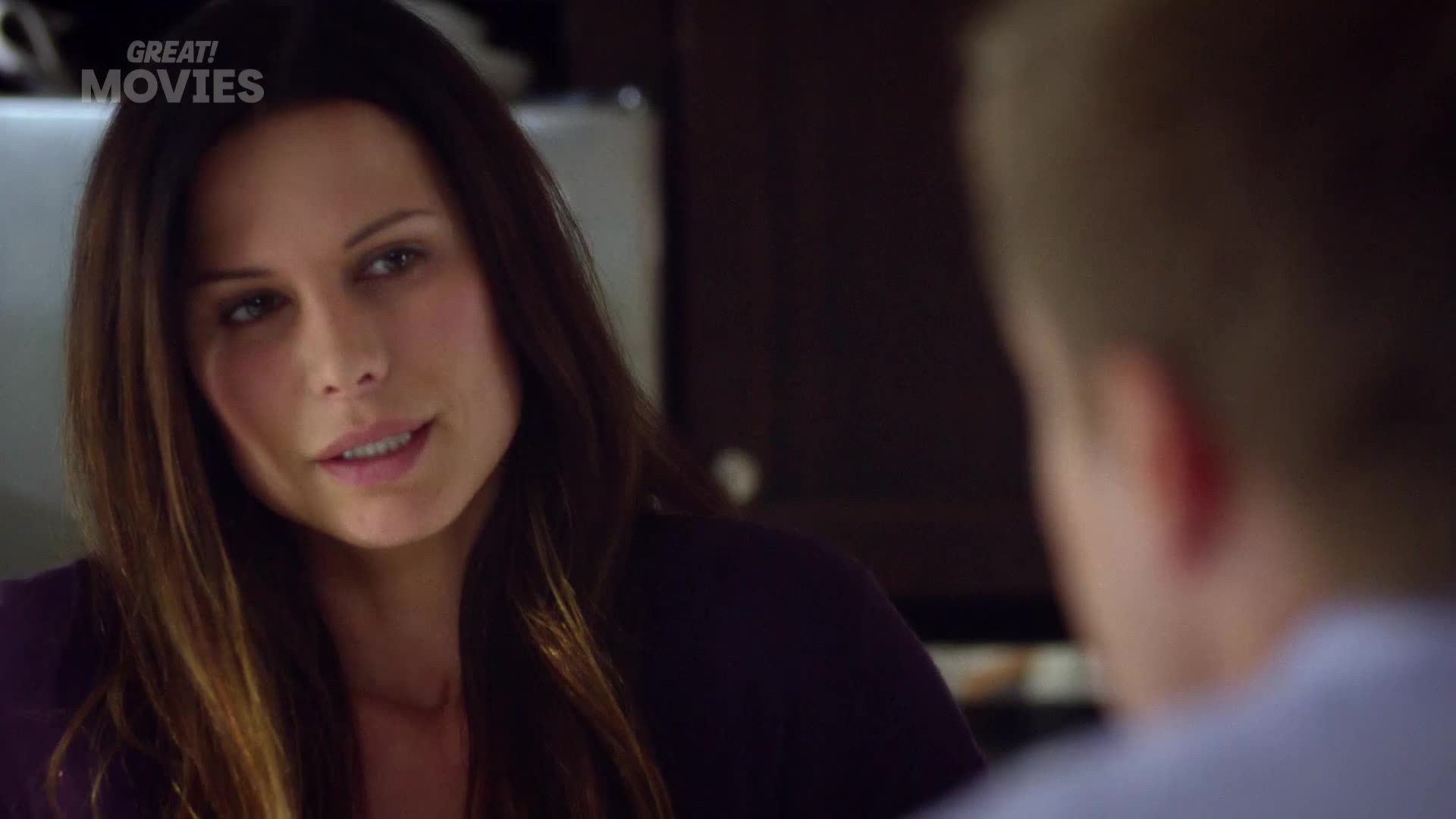 A woman with long, dark hair leans forward, speaking intently to someone out of frame. Her expression is serious, her lips slightly parted as if mid-sentence.