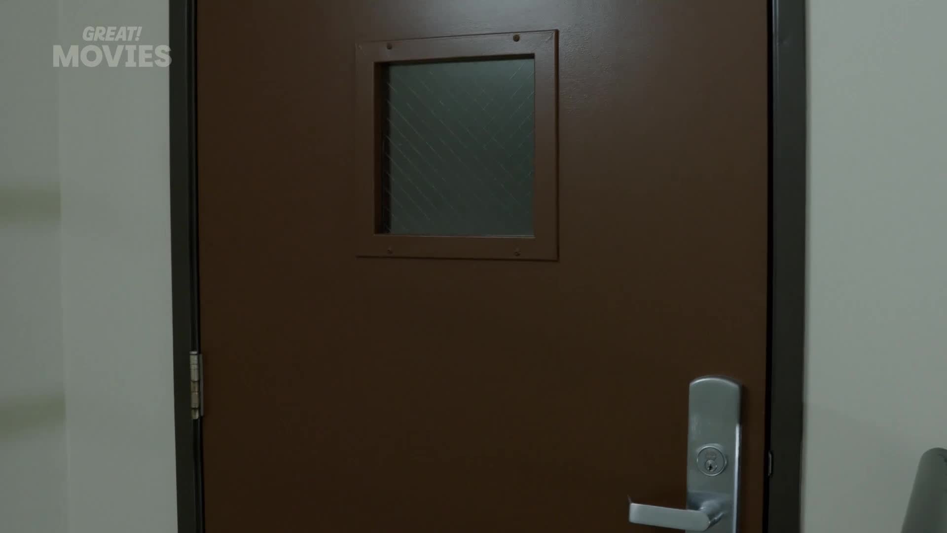 The door is a dark brown, with a small, square window set into it. A silver handle gleams on the right side.