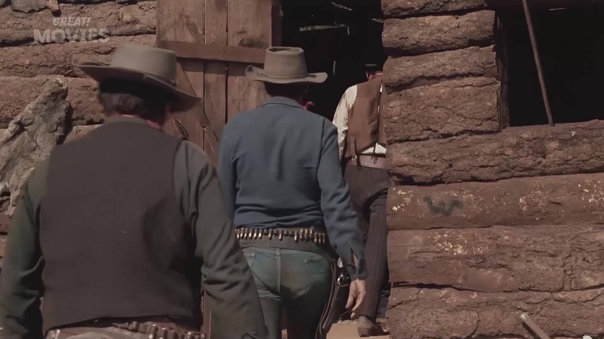 Three men in cowboy hats and vests walk into a rustic wooden building. One man's cartridge belt is clearly visible.