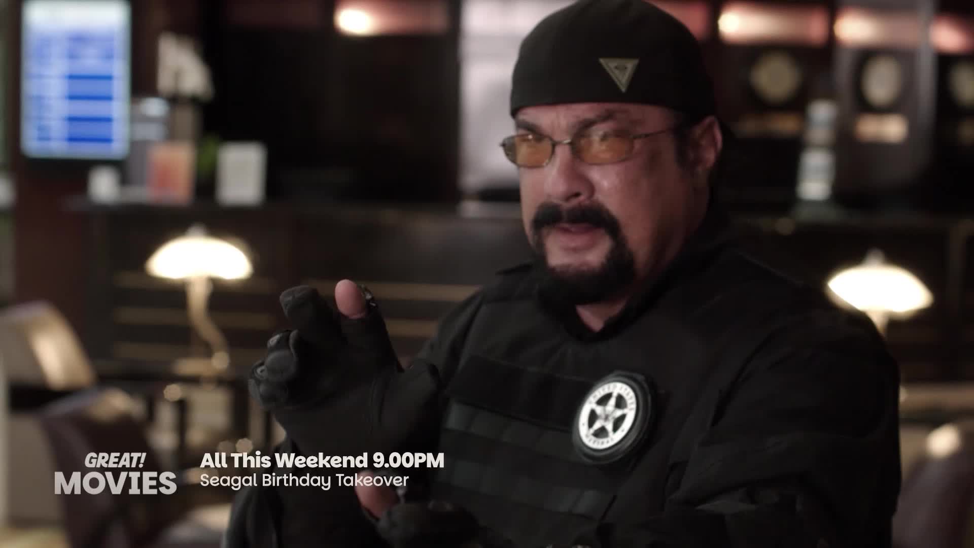 Steven Seagal, wearing a black beanie and tactical vest, gestures with his gloved hands. This weekend on GREAT! Movies, it's a "Seagal Birthday Takeover" starting at 9 PM.